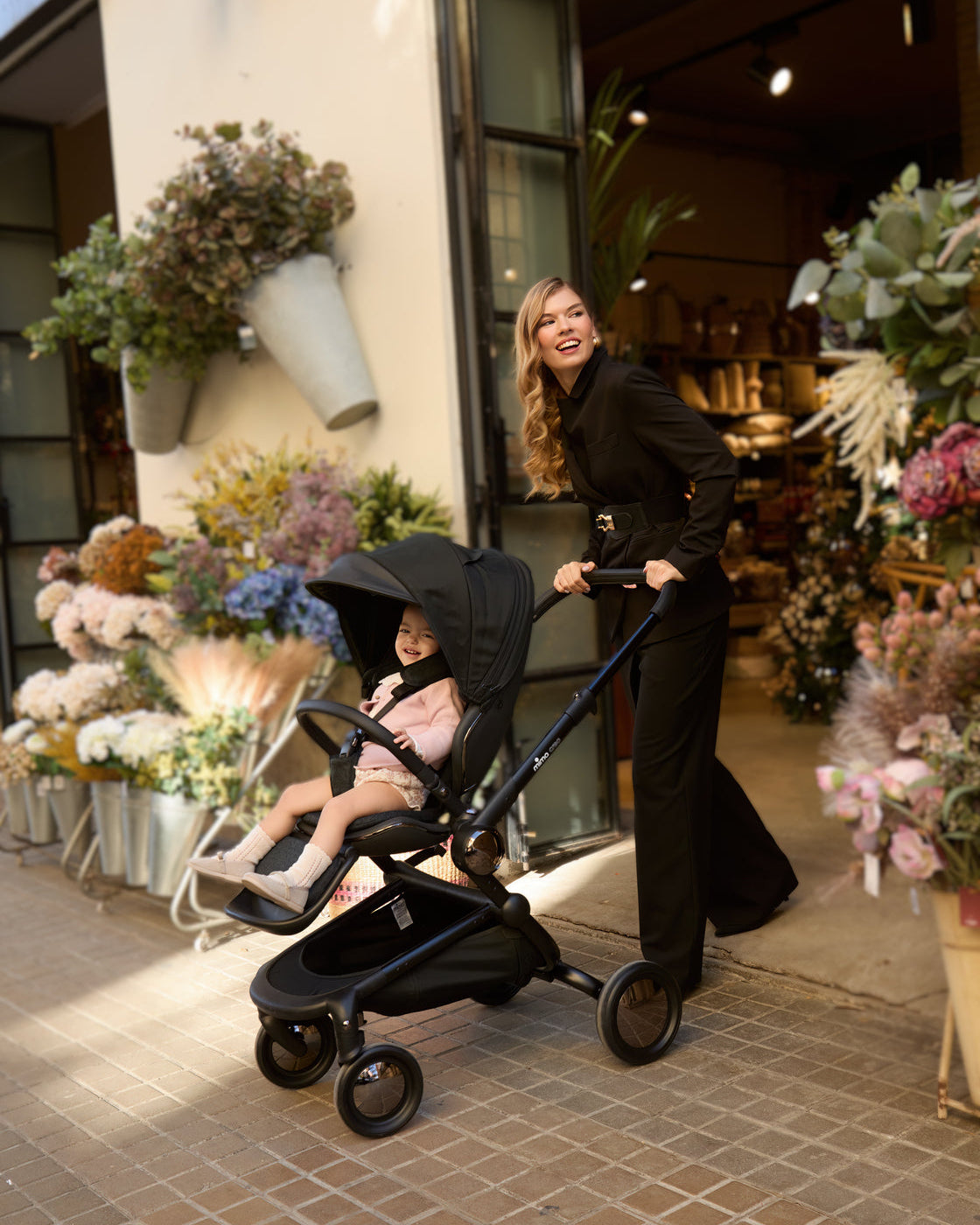 Woman pushing creo stroller in black in a city stroll exiting a flower shop.