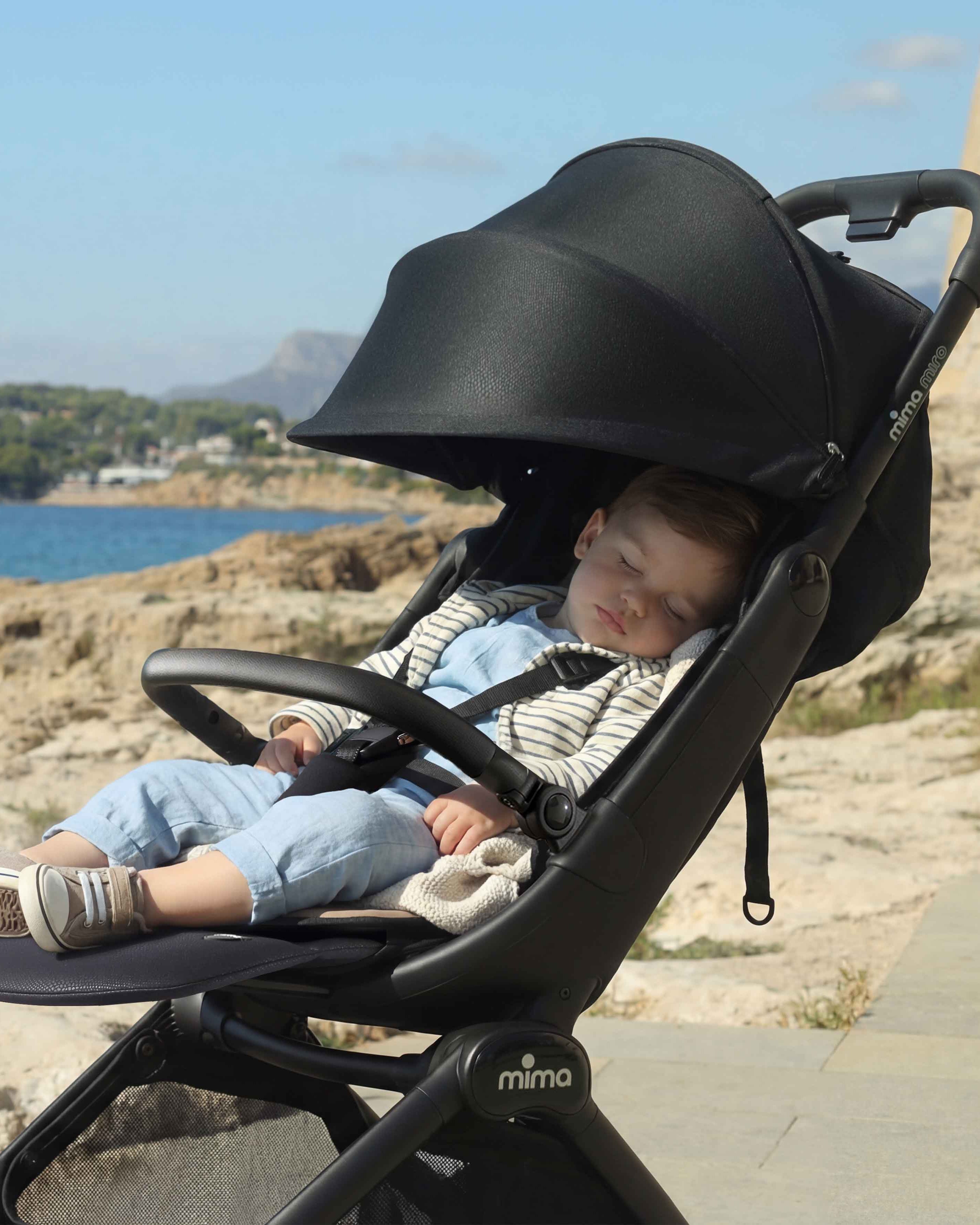 toddler sleeping in fully reclined mima miro stroller in black with extended canopy by the ocean