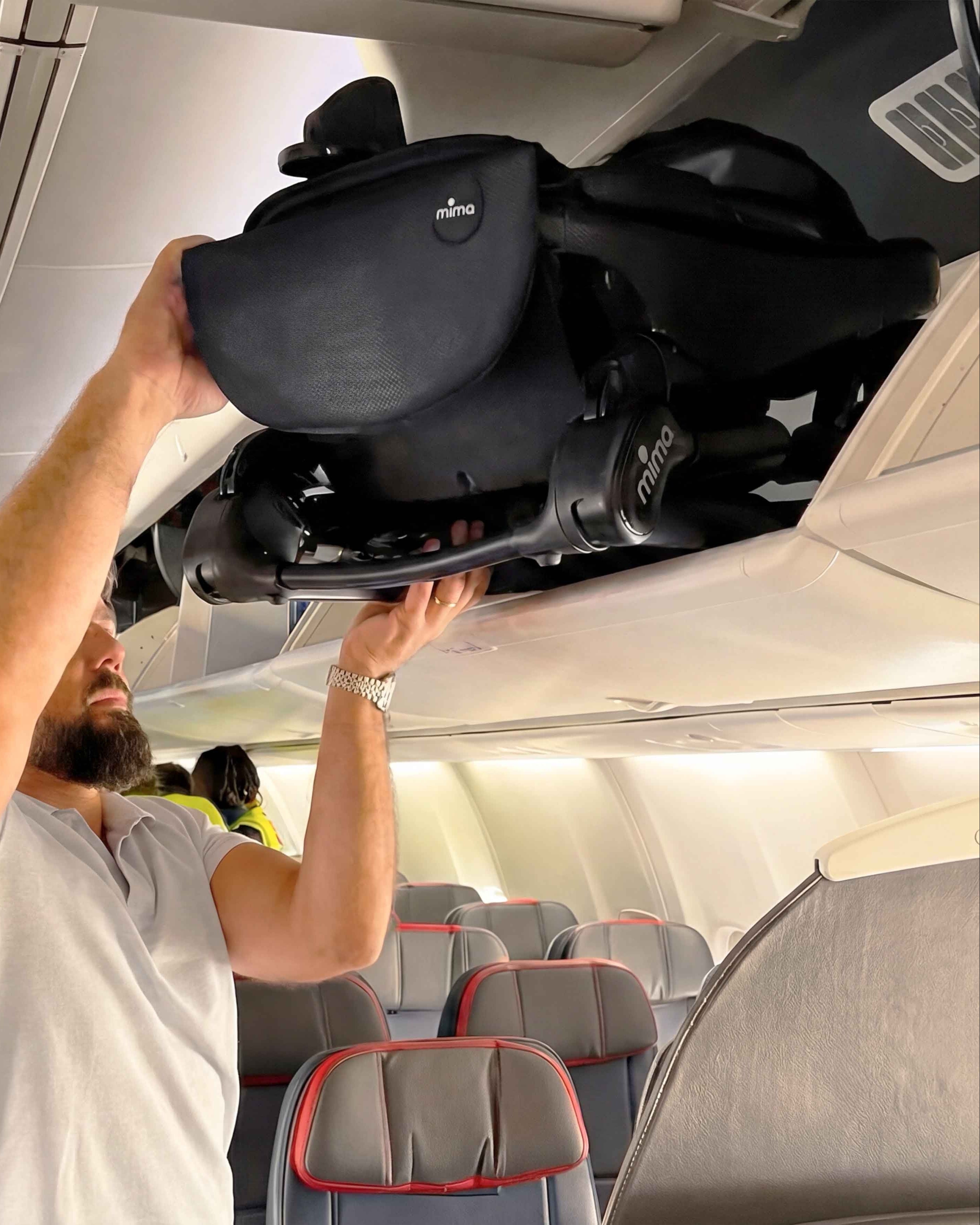 man placing folded mima miro stroller in black into an airplane overhead bin