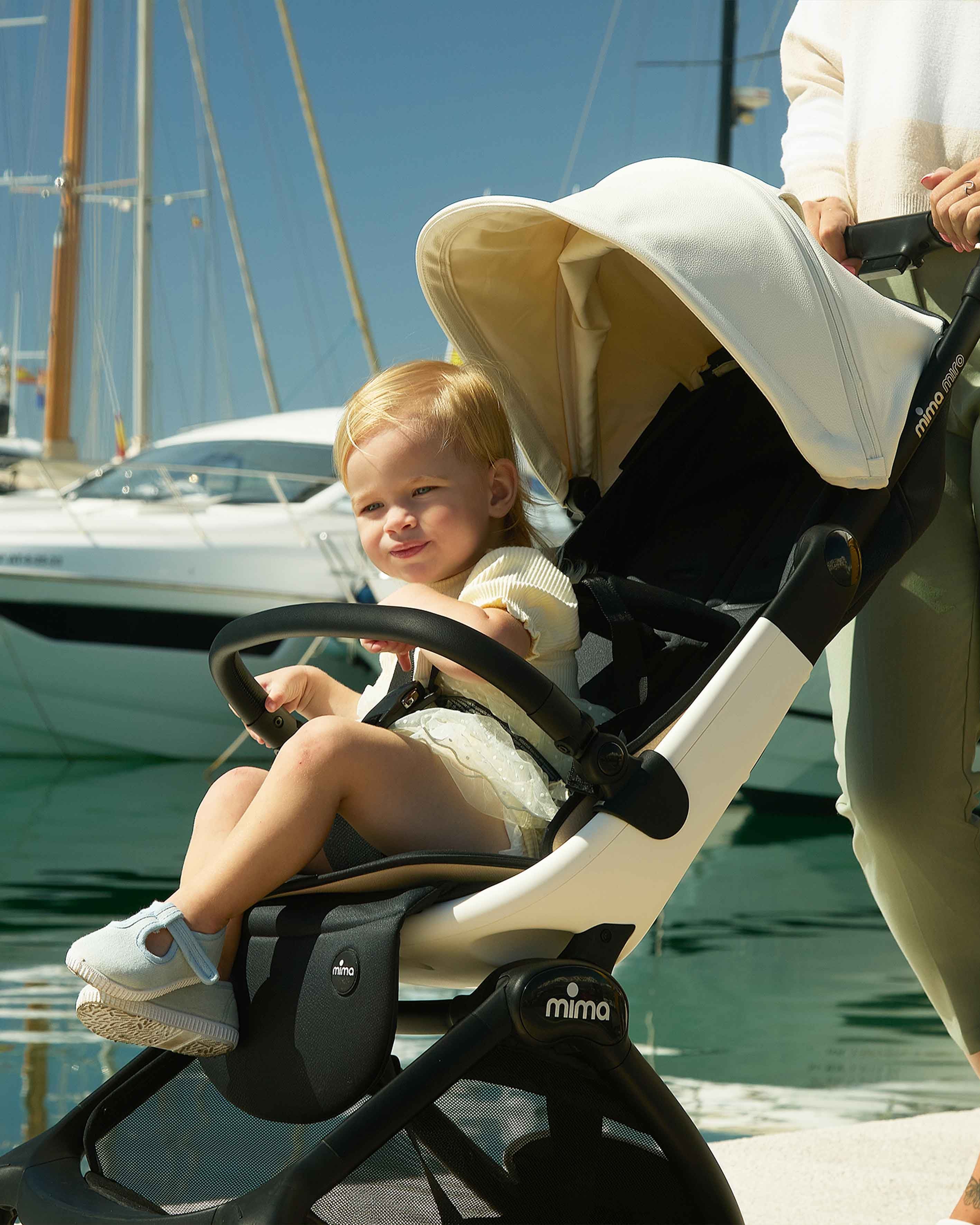 caregiver pushing miro compact travel stroller in white at a marina with yachts in the background