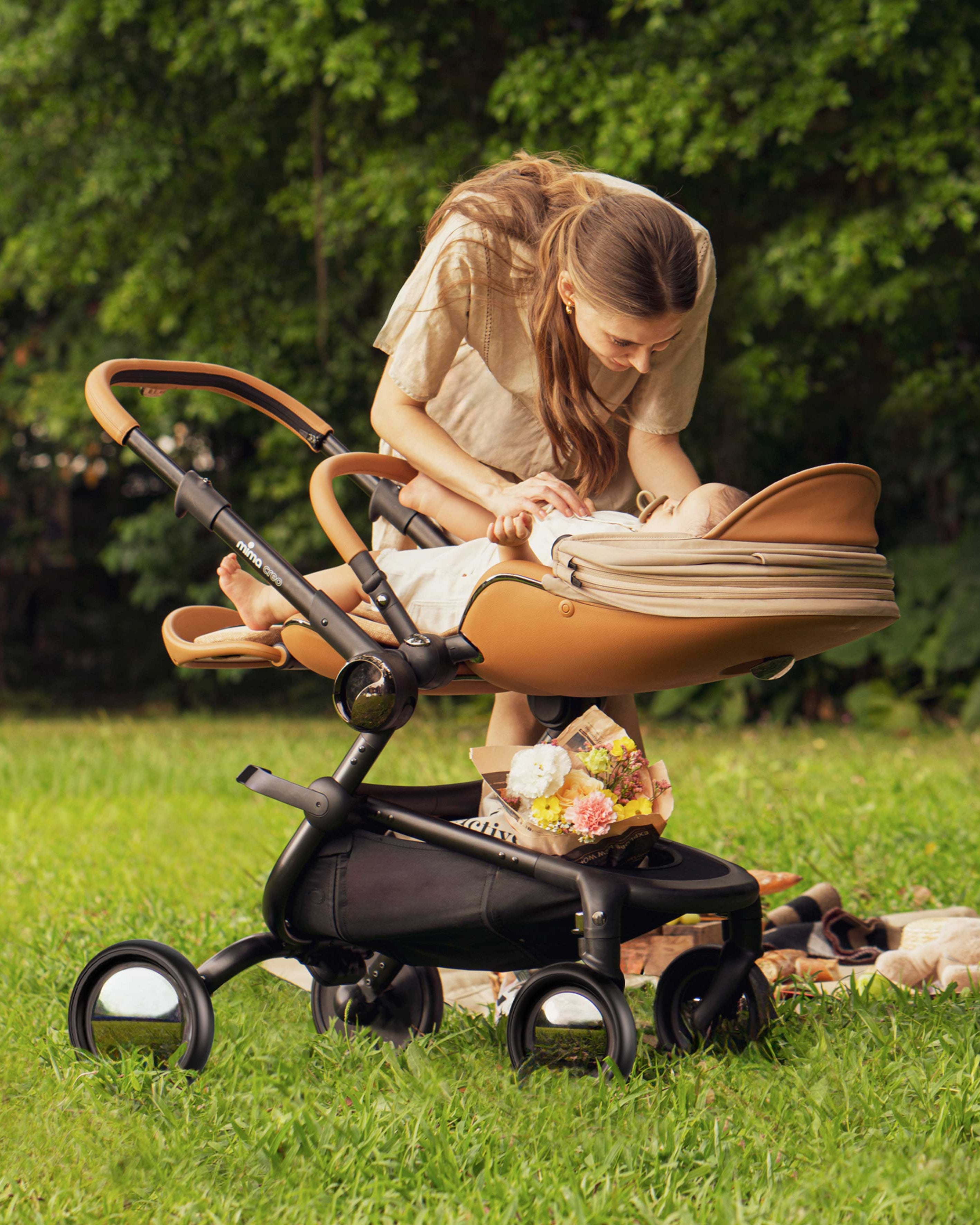 mother tending to baby in fully reclined parent facing mima creo stroller in mocha in a park