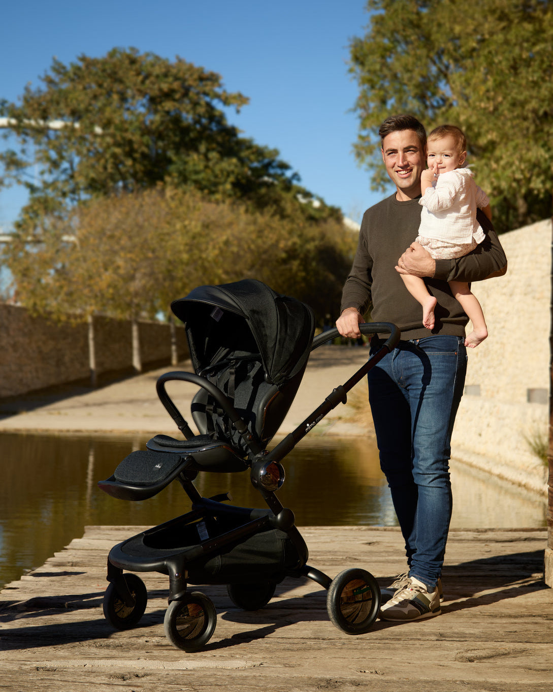 Parent holding the baby and pushing the creo stroller in black, to spend a perfect day in the park.